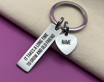 May include: Silver keyring with a heart-shaped charm that says "NAME" and a rectangular charm that says "It takes a long time to grow and old friend".