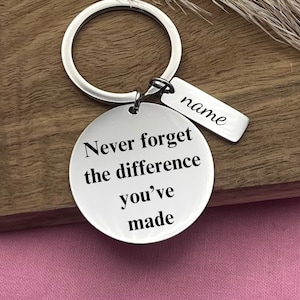 May include: Silver keychain with a round tag that reads "Never forget the difference you've made". A smaller tag with the word "name" is attached to the keychain.