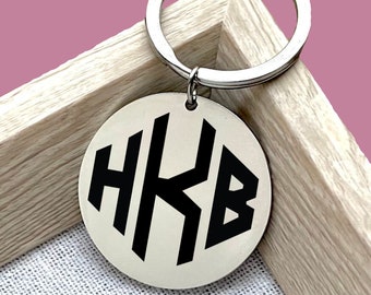 May include: A silver key chain with a round, silver charm featuring a black monogram of the letters "HKB".