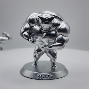 May include: A silver-colored figurine of Squirtle, a Pokemon character, in a muscular pose. The figurine is standing on a round base with the word "Squirtle" inscribed on it.