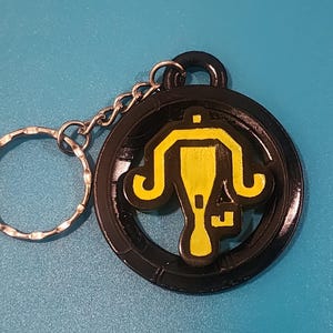 May include: A black metal keychain with a yellow graphic of a stylized lamp. The keychain has a silver ring.