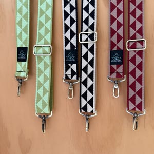 May include: Several patterned bag straps in various colors, including green, black and white, and burgundy. Each strap features a geometric design, metal hardware, and the "LO HAZEL" logo.
