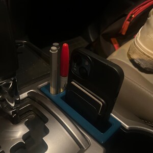 Könnte beinhalten: Ein blauer Plastik-Auto-Organizer mit einem Handyhalter, zwei Stiften und einem roten Stift.