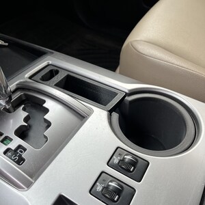 May include: A close-up of a car's centre console with a cup holder, gear shifter, and two knobs labelled "Def" and "Rear".