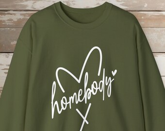 May include: Olive green sweatshirt with the word "homebody" in white script, inside a heart shape. The sweatshirt has long sleeves and a crew neck. The word "X" is below the word "homebody".