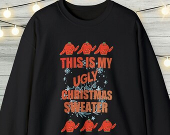 May include: Black sweatshirt with the text "THIS IS MY UGLY CHRISTMAS SWEATER" in orange and red. The design includes illustrations of red sweaters and snowflakes. A festive holiday apparel item.