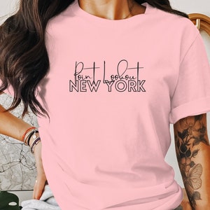 May include: A pink t-shirt with black text that reads "Bit about NEW YORK".