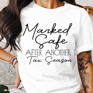May include: White t-shirt with black text that reads "Marked Safe After Another Tax Season".