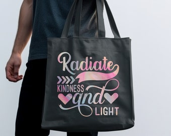 Könnte beinhalten: Eine schwarze Tragetasche mit einem rosa-blauen Aquarelldesign und dem Text "Radiate Kindness and Light" in Weiß.