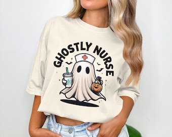 May include: Cream-coloured t-shirt featuring a cartoon ghost dressed as a nurse, holding a coffee cup and a pumpkin. The text "GHOSTLY NURSE" is printed above the ghost. Bats are also included in the design. Halloween themed.