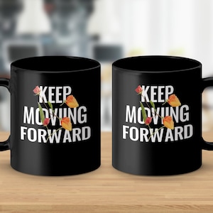 Puede incluir: Dos tazas de café negras con texto blanco que dice "Keep Moving Forward" y un diseño floral. Las flores son naranja y amarillas.