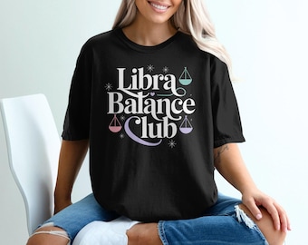 Può includere: T-shirt nero con la scritta "Libra Balance Club" in bianco, con bilance e stelle dai colori pastello. La maglietta è uno stile casual, a maniche corte.