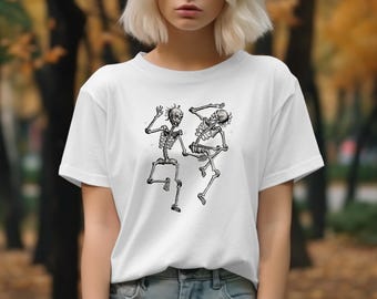 May include: White t-shirt featuring a black and white graphic of two dancing skeletons. The skeletons are depicted in a playful pose, with one raising an arm. The shirt is made of a soft material.