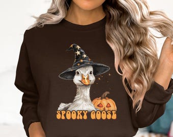 May include: A brown sweatshirt with a Halloween-themed design. It features a goose wearing a witch's hat and a carved pumpkin. The words "SPOOKY GOOSE" are printed below the image. A fun and festive design.