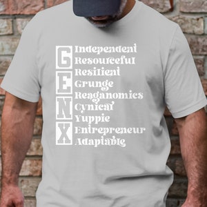 Könnte beinhalten: Ein graues T-Shirt mit weißem Text, der "Gen X" lautet und Eigenschaften der Generation X auflistet, darunter "Unabhängig, Ressourcenstark, Widerstandsfähig, Grunge, Reaganomics, Zynisch, Yuppie, Unternehmer, Anpassungsfähig".
