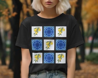 May include: Black t-shirt featuring a repeating pattern of blue and white tiles. Some tiles have a blue floral design, while others display a lemon branch with yellow fruit. The shirt is made of a soft material.