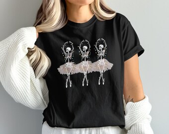 Può includere: T-shirt nero con grafica di tre ballerine scheletro in tutù. Gli scheletri sono in posa da balletto con le braccia alzate. I tutù sono rosa chiaro con accenti dorati. Un design unico e spettrale.