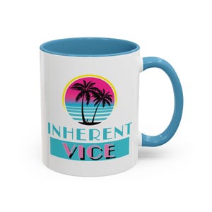 May include: White ceramic mug with a blue rim and handle. The mug features a graphic of palm trees and a sunset with the text "Inherent Vice" in a retro font.