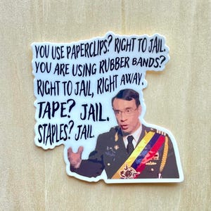 May include: A white sticker with the text "YOU USE PAPERCLIPS? RIGHT TO JAIL. YOU ARE USING RUBBER BANDS? RIGHT TO JAIL, RIGHT AWAY. TAPE? JAIL. STAPLES? JAIL." and a picture of a man in a military uniform.