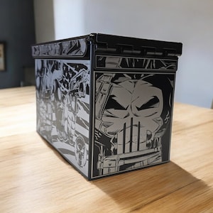 Peut inclure: Une boîte à munitions noire avec un graphique du crâne du Punisher et un fond de style bande dessinée.