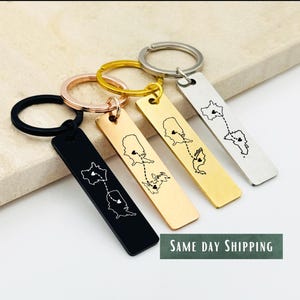 May include: Four rectangular keychains in black, rose gold, gold, and silver. Each keychain features a map design with a dotted line connecting two locations. The keychains are attached to metal key rings.