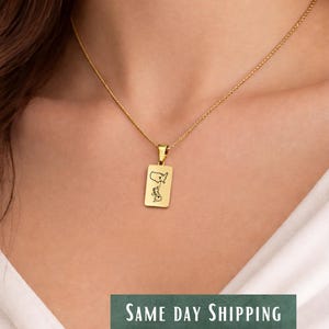 May include: Gold-colored pendant necklace featuring a rectangular pendant with a map design. The necklace is worn around the neck. The text "SAME DAY SHIPPING" is displayed on a green banner.