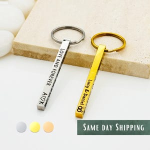 May include: Two silver and gold keychains with engraved bars. The silver keychain has the text "Love and Forever A♡K" engraved on the bar. The gold keychain has the text "Lucy & Daniel ∞" engraved on the bar.