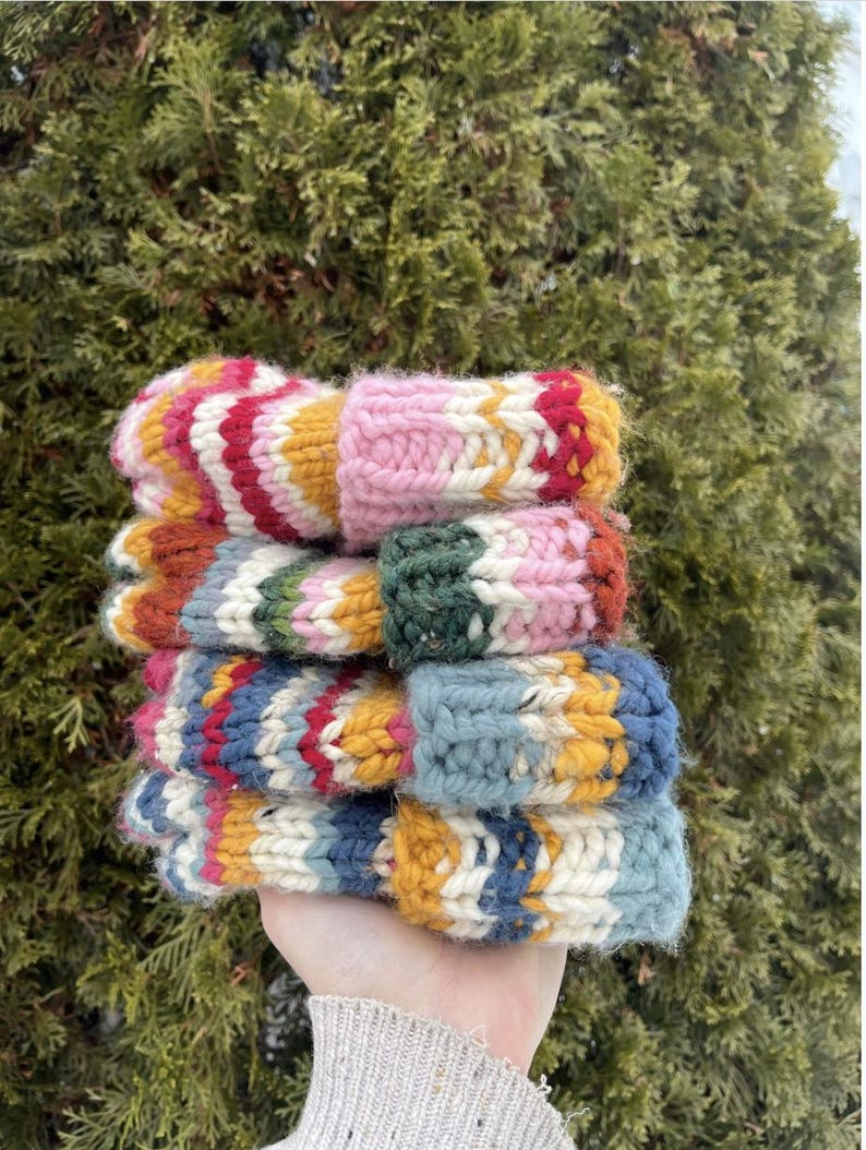 May include: A stack of four colourful knitted hats with stripes of pink, red, yellow, blue, green, and white.