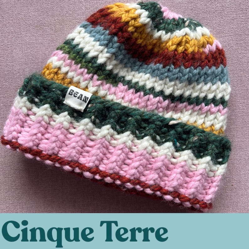May include: A colourful striped knitted beanie hat with a pink, white, green, and yellow pattern. The hat has a small white label with the word "BEAN" on it.