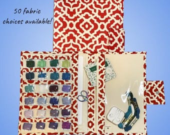 May include: A red and white patterned fabric organizer, open to display embroidery floss, scissors, and other craft supplies. The text "50 fabric choices available!" is visible. The organizer is designed to hold various craft items.