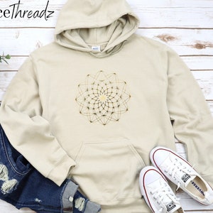 May include: A beige hoodie with a gold geometric mandala design on the front. The hoodie has a drawstring hood and a kangaroo pocket.