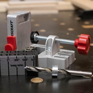 May include: A silver metal pocket hole jig with a black drill guide block and a drill bit. The jig has a red knob and lever. The drill guide block has measurements in inches.