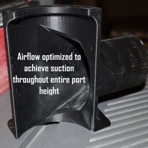 Pu&ograve; includere: Un collettore di polvere in plastica nera con un design curvo. Il testo "Airflow optimized to achieve suction throughout entire port height" &egrave; stampato sul collettore.