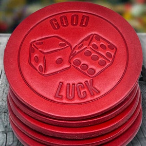 May include: A stack of four red leather coasters with a raised design of two dice and the words "GOOD LUCK".