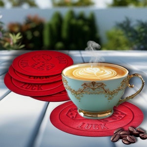 May include: Red leather coasters with the words "Good Luck" and a dice graphic. A cup of coffee sits on top of a coaster.