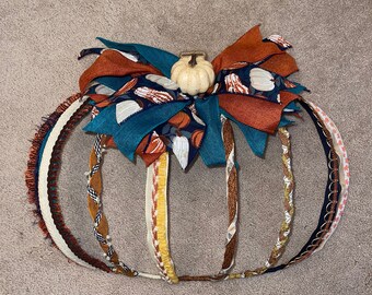 May include: A decorative pumpkin made from various ribbons and trims in shades of brown, orange, teal, and white. The pumpkin has a small white ceramic pumpkin on top.