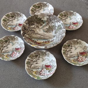 Könnte beinhalten: Ein Set aus sieben Keramikgeschirrstücken mit Landschaftsdesign. Das Set umfasst eine große Servierschüssel und sechs kleinere Schalen. Das Design zeigt Bäume, einen See und ein Haus mit rotem Dach, in einer Farbpalette aus Braun, Grün und Rosa.