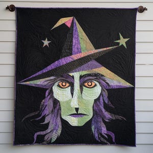 Könnte beinhalten: Ein rechteckiger Wandbehang mit einer zentralen Applikation eines Hexengesichts mit grüner Haut, violettem Haar und orangefarbenen Augen. Die Hexe trägt einen hohen, mehrfarbigen spitzen Hut mit zwei Sternen auf einem schwarzen Hintergrund.