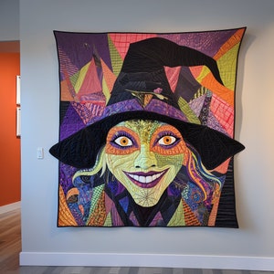 May include: A colorful patchwork quilt featuring a witch with a green face and a wide smile. The witch is wearing a black hat with a purple brim and a long, flowing purple and orange dress. The quilt is made up of various fabrics in shades of green, orange, purple, and black.