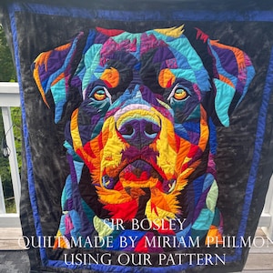Puede incluir: Un edredón colorido con un retrato de perro Rottweiler. La cara del perro está compuesta por formas geométricas en tonos de azul, morado, naranja y amarillo sobre un fondo negro. El edredón tiene un borde azul e incluye el texto "SIR BOSLEY" y "QUILT MADE BY MIRIAM PHILMON USING OUR PATTERN."