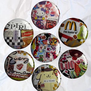 May include: A collection of seven round, colorful button pins with various designs. One features Hello Kitty, another says "I'm lovin' it", and others have text like "Y2K" and "HK & FRIENDS". The pins are arranged on a white, textured surface.