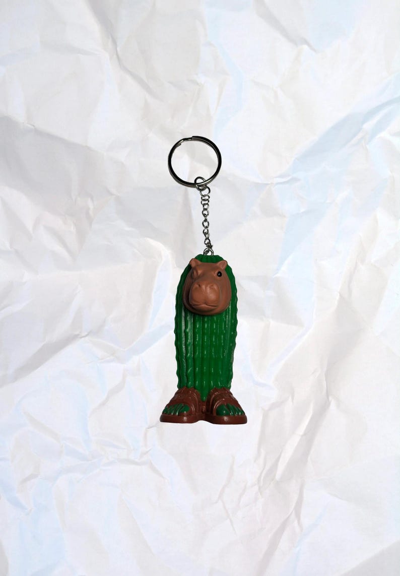 Puede incluir: Un llavero novedoso con una figura caprichosa verde, parecida a un cactus, con cabeza y pies de hipop&oacute;tamo marr&oacute;n. El llavero tiene un anillo y una cadena de color plateado. La figura mide aproximadamente 7,6 cm de alto.