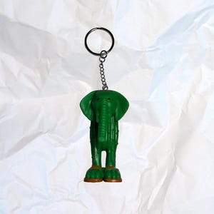Puede incluir: Llavero de elefante verde con cadena y anilla plateadas. El elefante tiene patas marrones y un cuerpo texturizado. Un accesorio divertido para llaves o bolsos.