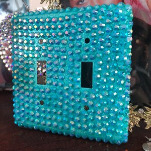 May include: A turquoise blue light switch cover with a double switch, completely covered in iridescent rhinestones.
