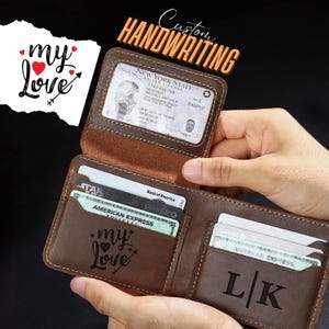 May include: A brown leather bi-fold wallet featuring a clear ID window, multiple card slots, and custom laser-engraved text. The interior displays the phrase "my love" with a heart and arrow graphic, along with the initials "L K" on the right side.