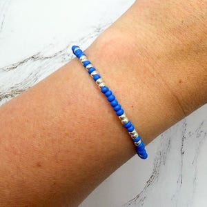 May include: A delicate bracelet featuring a repeating pattern of small, vibrant blue beads and polished silver-toned metallic beads. The circular beads are strung together in a single strand, creating a simple and uniform design around the wrist.