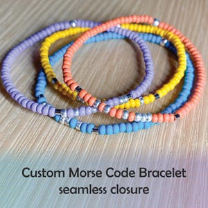 May include: A multi-colored beaded bracelet with a seamless closure. The bracelet is made with purple, blue, yellow, and orange beads.  Custom Morse Code Bracelet seamless closure.
