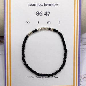 May include: A black beaded bracelet with silver beads, displayed on a card that reads "seamless bracelet" and "86 47". The card has a purple border with yellow and white accents. Sizes XS, S, M, and L are listed.