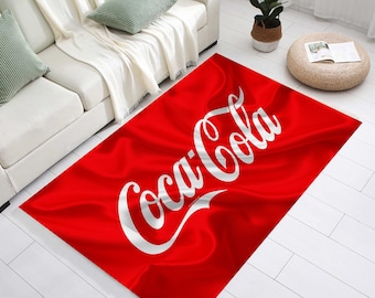 Könnte beinhalten: Ein rechteckiger roter Teppich mit dem Coca-Cola-Logo in weißer Schrift. Der Teppich hat eine wellenförmige, stoffartige Textur und liegt auf einem weißen Boden. Ein dekoratives Wohnaccessoire.