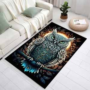 Puede incluir: Una alfombra negra con una ilustraci&oacute;n detallada de un b&uacute;ho azul y blanco posado en una rama. El b&uacute;ho tiene grandes ojos amarillos y patrones intrincados en sus plumas. El fondo presenta una luna dorada y follaje oscuro.